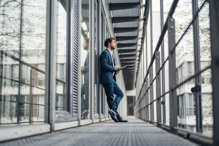 Thoughtful businessman with digital tablet standing at office corridor