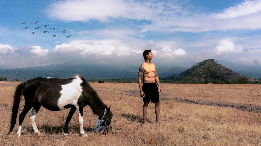 Shirtless man standing by horse on field