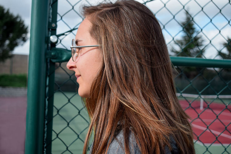 Side view of teenage girl standing by fence at court