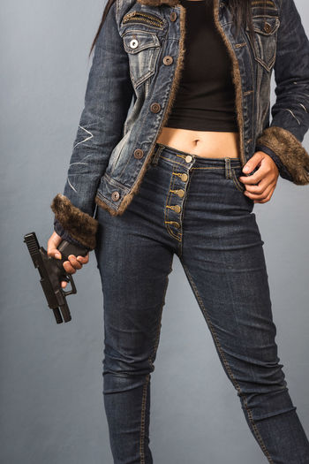 Midsection of woman holding handgun while standing by wall