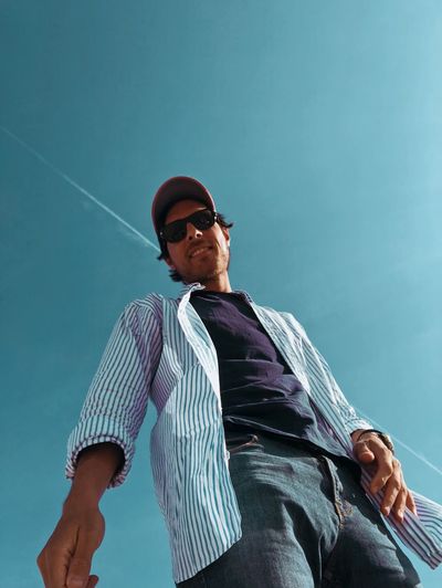 Low angle portrait of man in sunglasses standing against blue sky