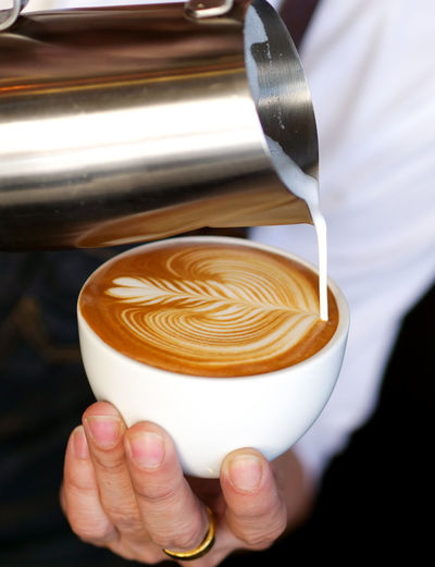 Midsection of barista pouring cream in coffee at cafe