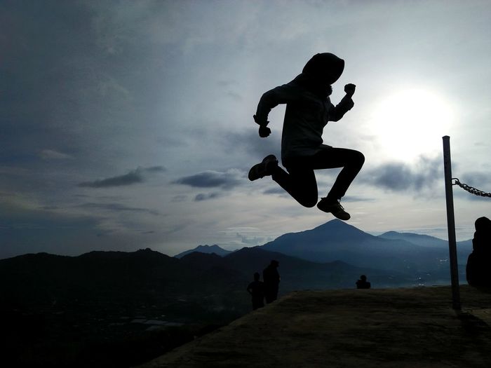 Silhouette man jumping on mountain against sky