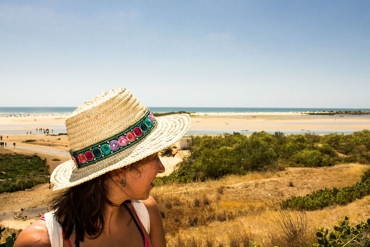 Woman wearing sun hat at beach against sky