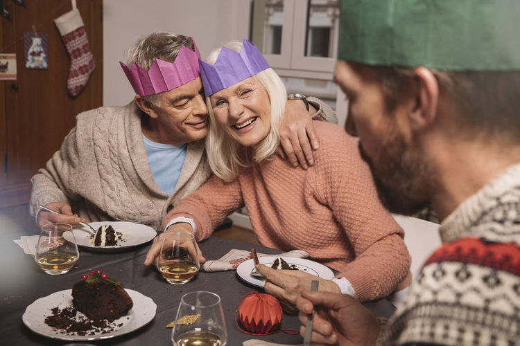Happy senior couple with paper crowns having christmas pudding
