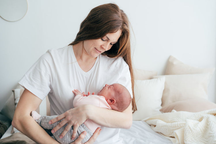 Young attractive mother holds and hugs her newborn daughter.
