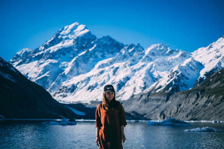 Young girl standing next lake shore with snowcapped mountain at the back.