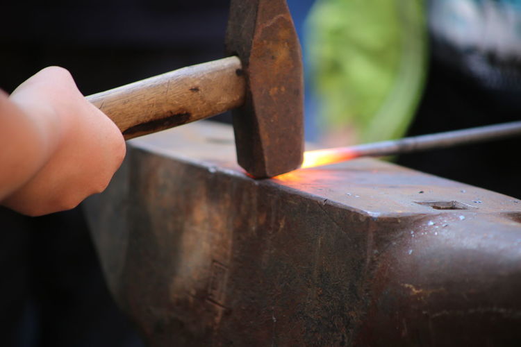 Cropped hand of worker hammering metal on anvil at factory