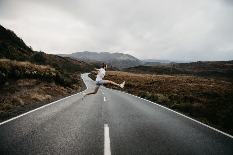 Man jumping on road against sky