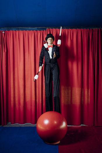 Male artist juggling pins while standing on stilts at circus