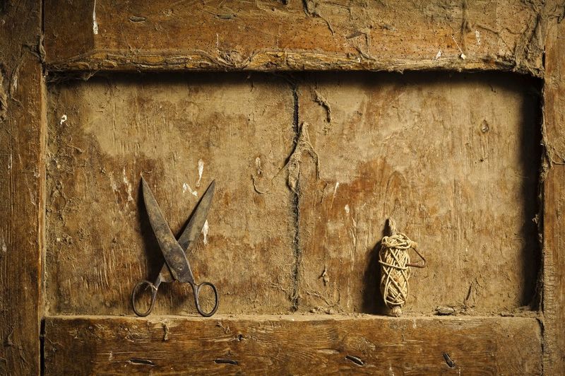 Close-up of rusty scissors and thread on dirty wooden niche