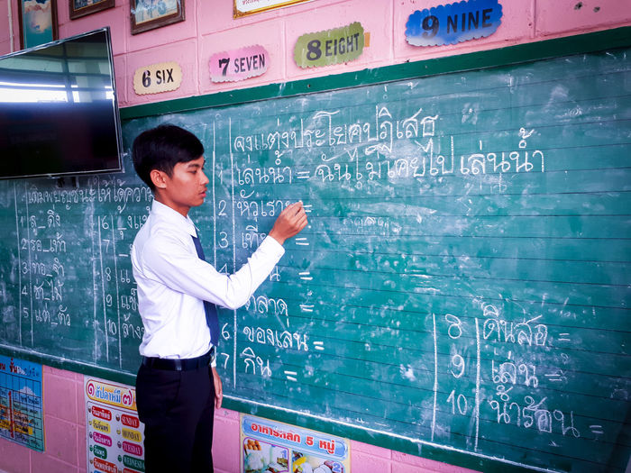 Side view of young man writing formula on blackboard in classroom