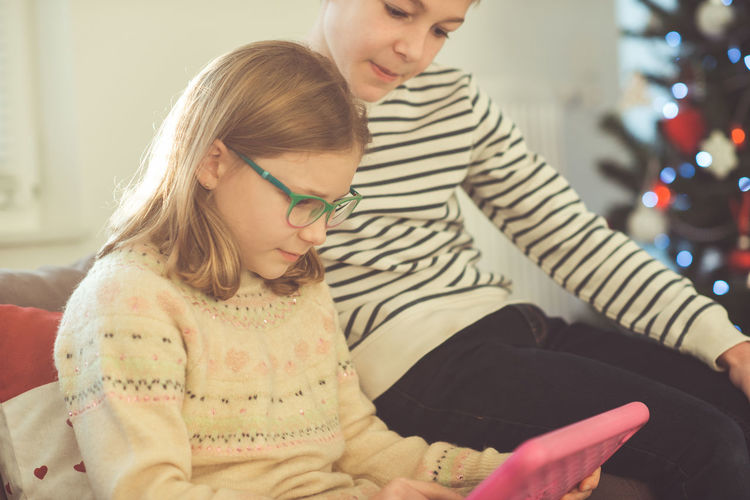 Siblings using digital tablet at home during christmas