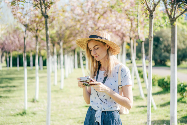 Young woman using phone while standing on plants
