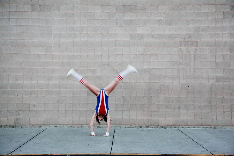 Woman in old-fashioned sports costume doing cartwheel on sidewalk against wall