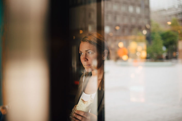 Mature businesswoman eating wrap sandwich in cafe seen from window