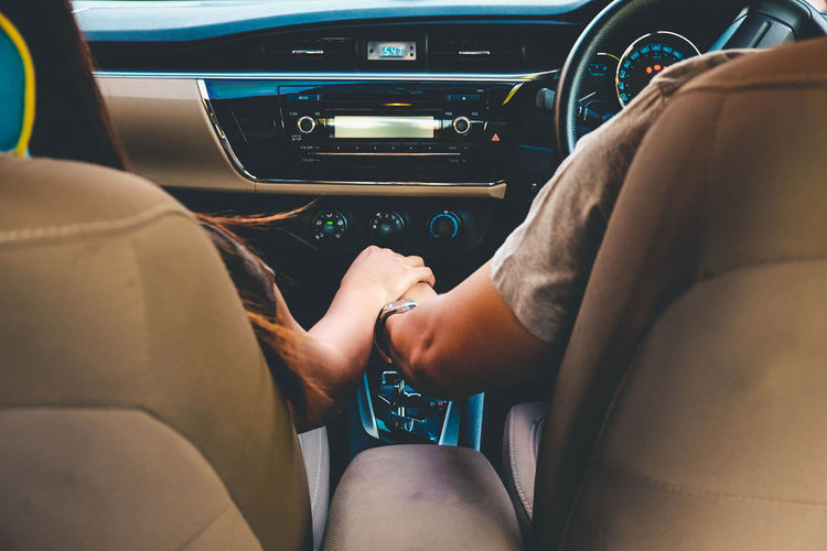 Midsection of couple holding hands in car