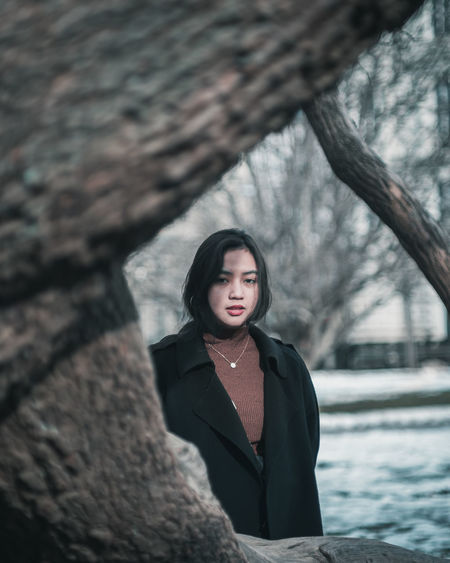 Portrait of young woman seen though tree standing outdoors during winter