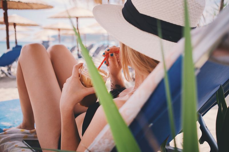 Woman drinking coffee while relaxing on lounge chair at beach