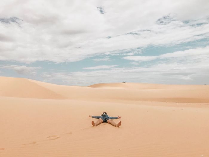 Man lying at desert against cloudy sky
