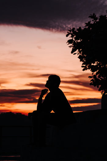 Silhouette man sitting against dramatic sky during sunset