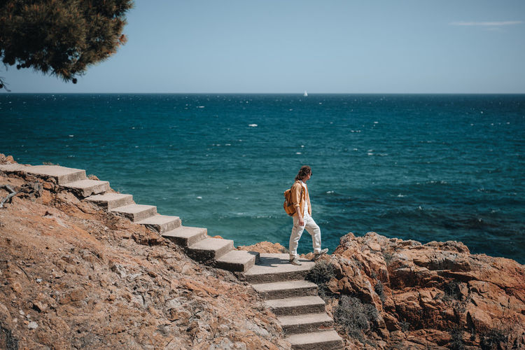 A traveler with long hair stands on stairs and looking to the deep blue sea. travel and hiking. 