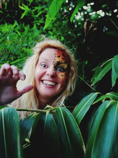 Portrait of smiling woman with face paint standing by plant leaves