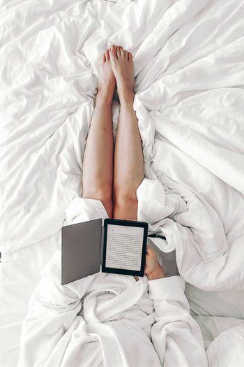 High angle view of woman lying on bed with a book