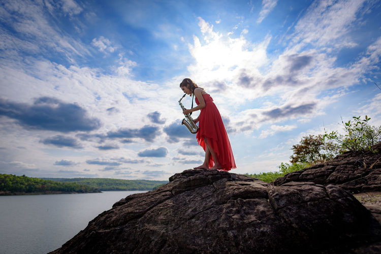 Woman playing musical equipment at lakeshore against sky