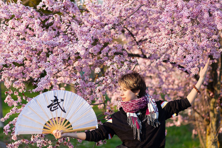 Young caucasian woman posing a wushu martial art posture in a sunny day, a pink tree in background