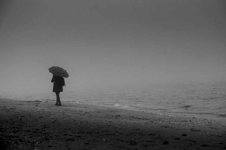 Rear view of woman standing on beach against sky