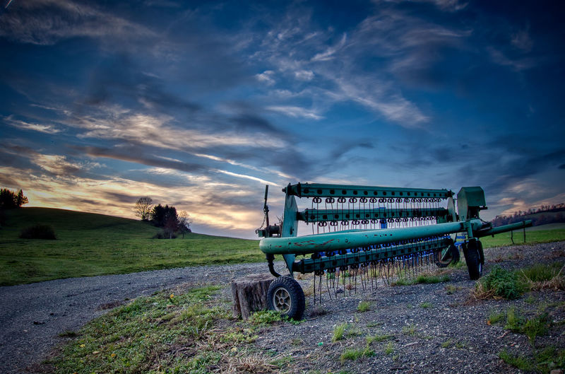 Agricultural machinery on land against sky during sunset
