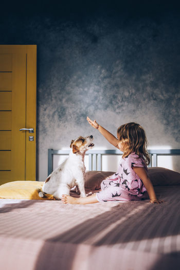 Girl playing with dog on bed at home