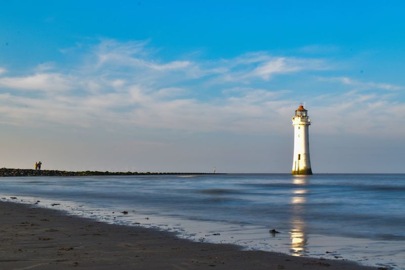 Lighthouse on beach by sea against sky