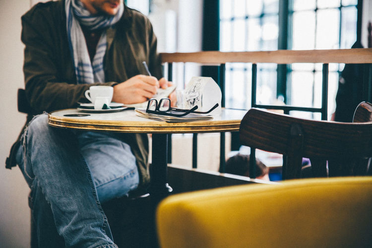 Man writing while sitting on chair in cafe