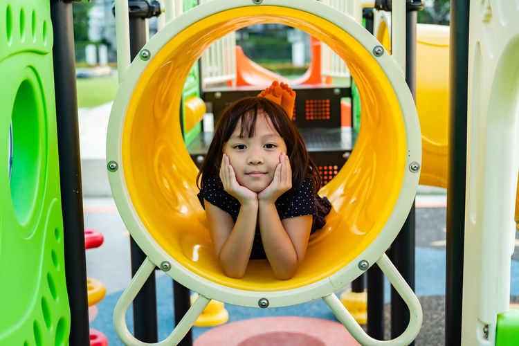 Portrait of smiling cute girl lying on outdoor play equipment in playground