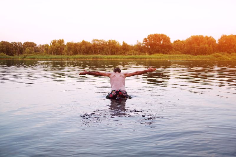 Full length of shirtless man in lake against sky
