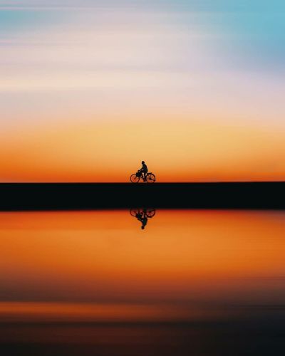 Silhouette person in sea against sky during sunset