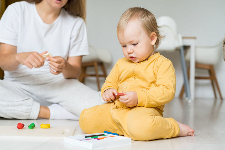 Adorable baby playing with modeling clay on floor. faceless mother promoting child development