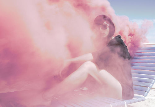 Young woman on sun lounger in pink smoke