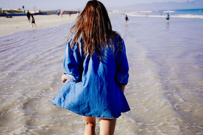 Rear view of woman with brown hair walking on sea shore at beach