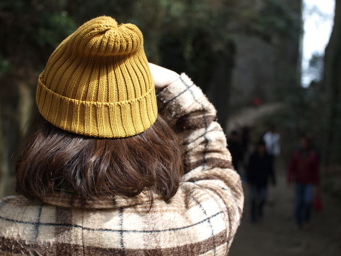 Rear view of woman with short brown hair wearing yellow knit hat standing at park