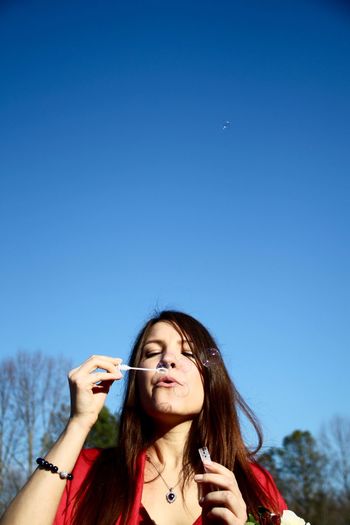 Young woman blowing bubbles against clear blue sky