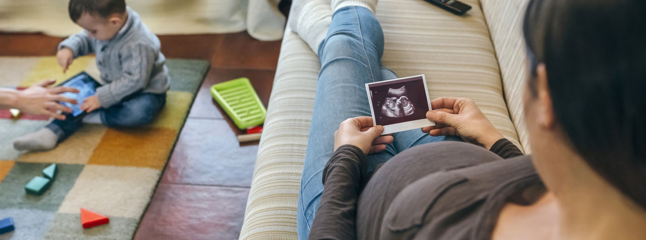 Mother holding ultrasound while father using digital tablet with son in living room