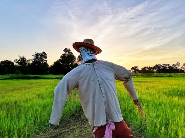 Scarecrow on agricultural field against sky during sunset