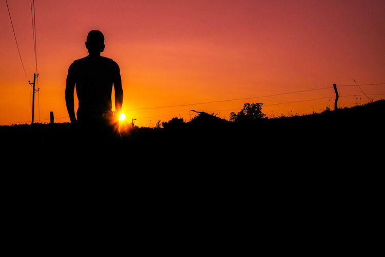Low angle view of silhouette man standing against orange sky during sunset
