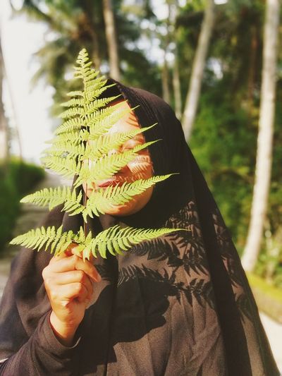 Close-up of woman holding fern over face