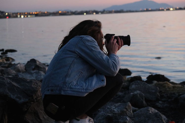 Midsection of woman photographing on rock at beach