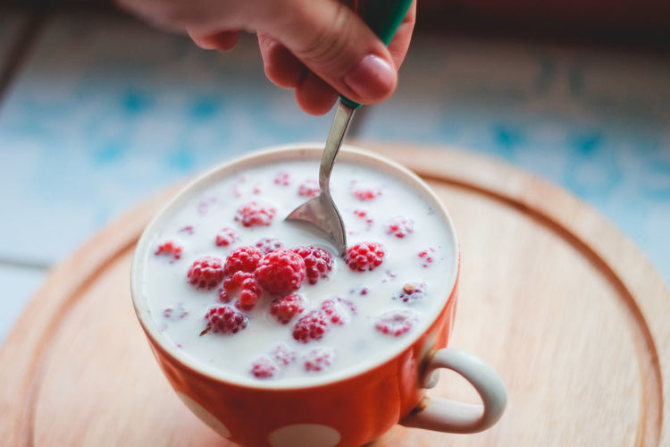 Close-up of hand stirring milk and berries in cup