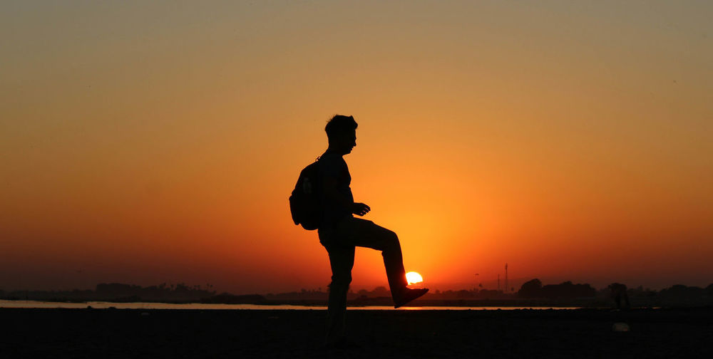 Side view of silhouette man standing against orange sky